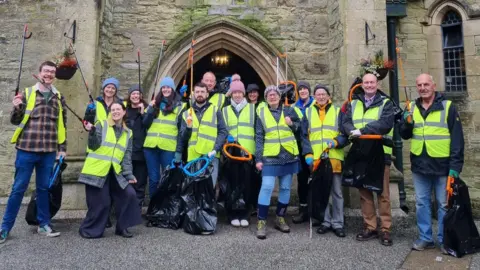 A group of volunteers stood together wearing high-visibility jackets, holding bin bags and litter picks.