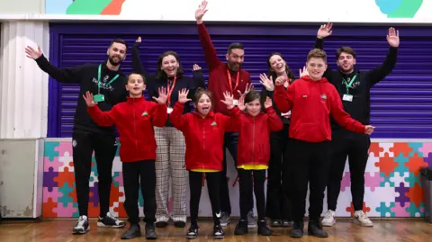 Bristol City Robins Foundation A group of school pupils from Ashton Vale Primary School stand on stage with their arms raised and smiling along with staff from Bristol City during a presentation about preserving wildlife