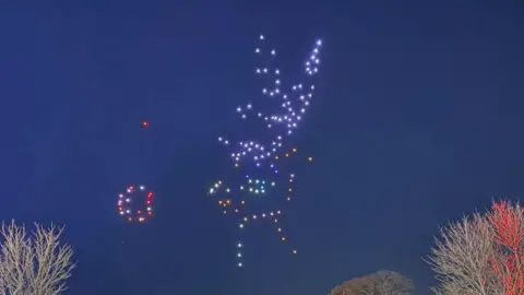 Abbie Louise Homer People standing in the Ardingly South of England showground look at an image of a reindeer created in the sky by drones.