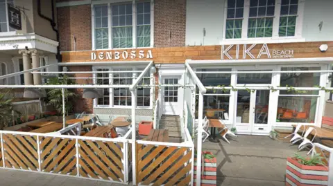 An exterior scene of the deserted Kika Beach bar with wooden outside seating.