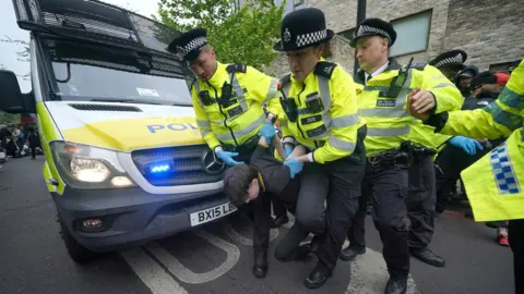 PA Media Police remove a protester after demonstrators formed a blockade around a coach