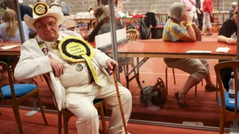 PA Alan Hope has a white stetson, suri, waistcoat and shirt and is seen here seated at the Wakefield by-election count in 2022.