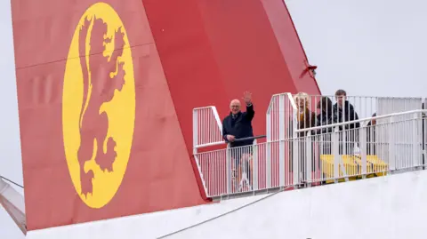 PA Media John Swinney, waving, on the deck of a CalMac ferry.