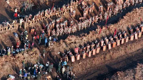 Forestry England An aerial shot of rows of extras dressed as soldiers, carrying swords and shields, with a large filming crew to the side of the field.