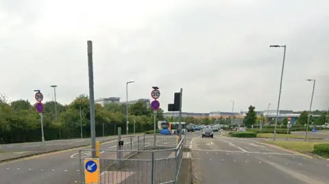 Google Google street view image of the traffic lights on the road, with the main hospital building seen in the distance.