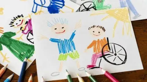 West Berkshire Council Child's colourful drawing showing two children, one using a wheelchair, surrounded by coloured pencils on a wooden table.
