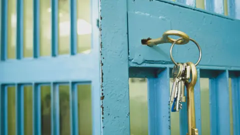 Getty Images A brass key in the lock of a prison door, with the metal bars painted light blue.