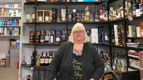 SImon Spark/BBC A blonde-haired Shelley Williams standing in front of a row of shelves filled with whisky