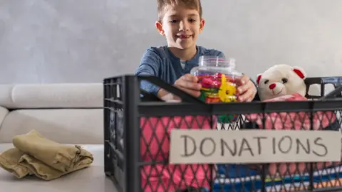 Getty Images Young boy packing clothes, toys and a teddy bear in a donation box.