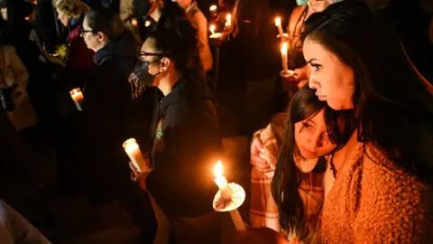 Getty Images Photo of a woman and a child during a candlelight vigil in California on Tuesday, in the aftermath of three mass shootings in the state