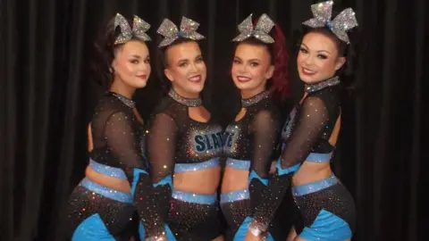 (L-R) Karen Breslin, Orla McConnell, Clodagh McGonagle and Megan Moore. They are all their cheer uniforms with big silver bows in their hair and blue and black costumes. 