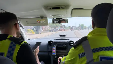 Two male police officers drive through the streets of Scunthorpe. The photo has been taken from the back seat of the police car.