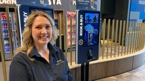 James Grant/BBC A woman smiling a the camera in a cinema foyer
