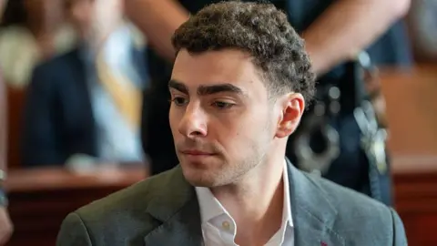 Getty Images Luigi Mangione is seen from the shoulders up, sitting at the defence table in court. He wears a charcoal grey suit.