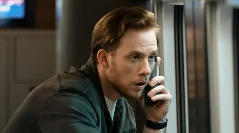 Joe Cole as Joe Roag in Nightsleeper, seen talking on a satellite phone on the train