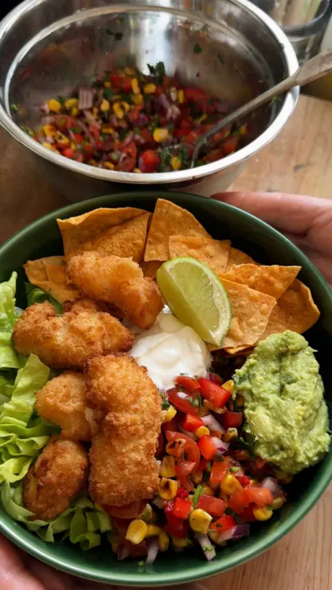 Two bowls, one silver one with salad inside and a green bowl of scampi, salad and tortilla chips.