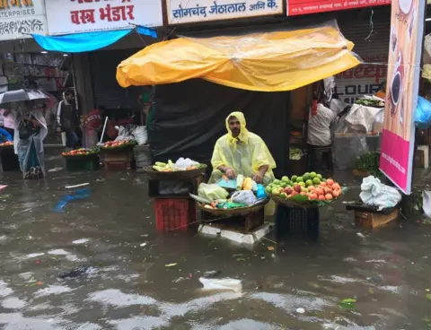 BBC A vegetable seller sits at his stall, amid a flood left by the heavy rains in Mumbai.