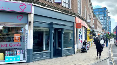 David Freezer/BBC A row of shops on a city centre street corner. The middle shop is vacant, with a painted blue-grey frontage.