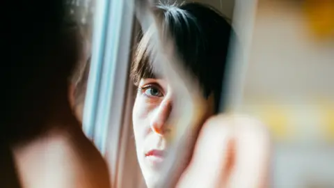 Young woman looks into a broken mirror