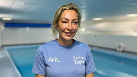 Tom Jackson/BBC Billie, a woman in a purple T-shirt, smiling for the camera, while standing in front of a swimming pool.