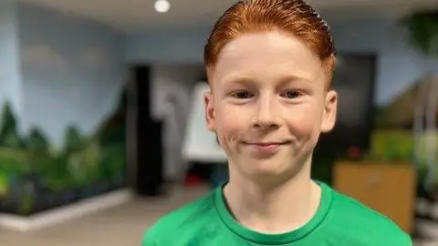 Will is pictured smiling at the camera. He has red hair and a green t-shirt