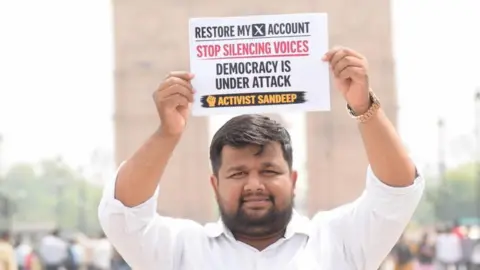 Sandeep Singh, an X user, holds up a placard saying 'Restore my X account. Stop silencing voices. Democracy under attack' on a street in India