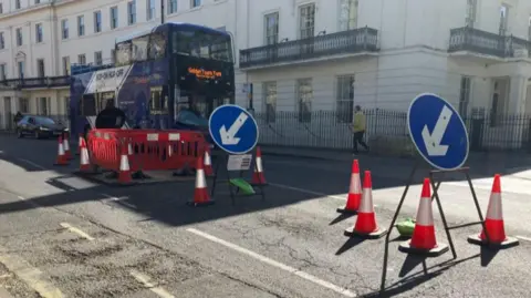 Red tourist bus waiting at roadworks on St Leonard's Place in York