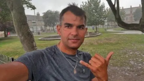 Tancredo Bankhardt standing outside taking a selfie. He is looking directly at the camera and is wearing a grey T-shirt.