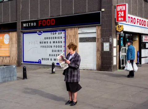 Peter Dench A woman reads The Daily Mirror newspaper. Archway, London.