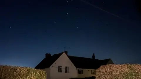 A white house with a brown roof. The sky has several stars in it 