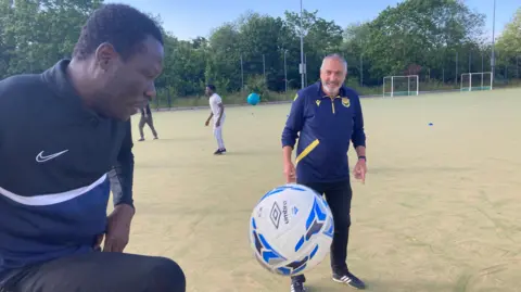 BBC Player taking a touch of the football, with a coach looking on