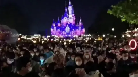 Mask wearing crowds in front of iconic Disney castle