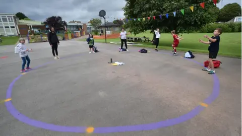 PA Media Children dance on a measured and painted socially distanced circle in the playground as they wait to be picked up by their parents at Llanishen Fach Primary School in Cardiff