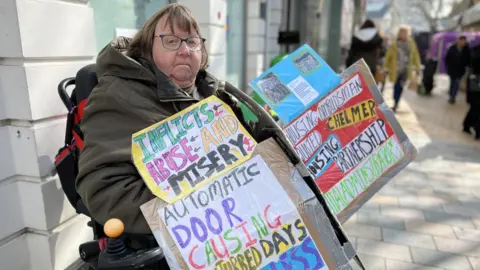 Carol Aldridge on Chelmsford High Street with protest banners.