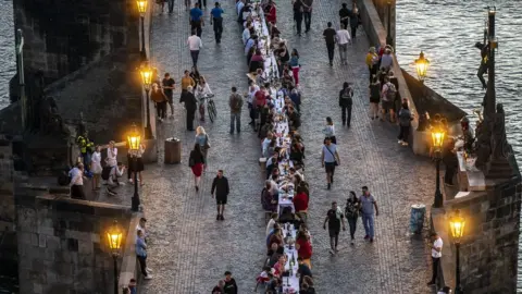 Getty Images People sit at a long table on the Charles Bridge