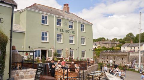 The Pier House pub with customers sat around outdoor tables and Charlestown harbour in the background