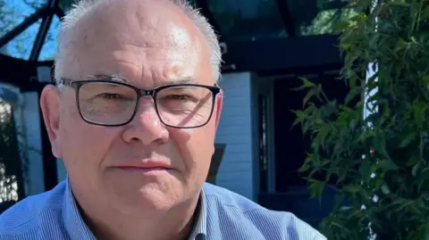 A man in a blue shirt and glasses looks at the camera