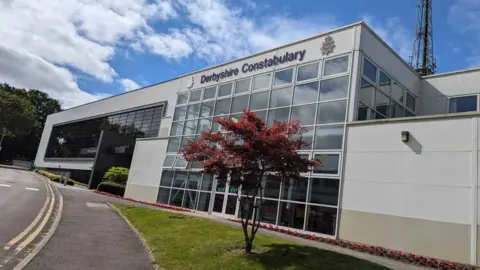 Derbyshire Police HQ is pictured. It is a multi-storey building with many windows. Derbyshire Constabulary logo is on the top of the building.