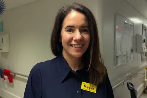 Megan Tjasink, a woman was long brown hair, wearing a navy collared top and a bright yellow name badge that says Megan on it