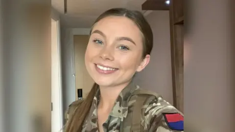 Gunner Jaysley Beck smiles in a selfie wearing a khaki camouflage jacket.