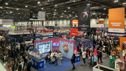 Thomas Copeland / BBC News A view of a full expo hall, with hundreds of people milling about between colourful branded stalls.