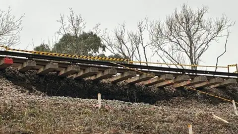 A view from below of the landslip, which shows shows the track dangling in the air and no land supporting it.