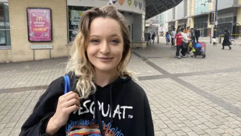 BBC Amy Richardson wearing a hoodie and holding a tote bag outside the Birmingham Bull Ring Indoor Market. 