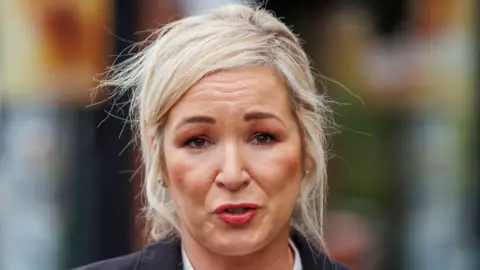 PA Media First Minister Michelle O'Neill, pictured from the shoulders up, with blonde hair, tied up. 