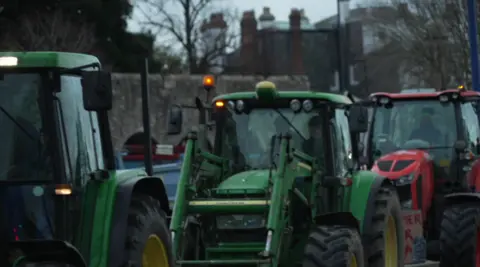 Image of a green tractor in Southampton with yellow and black tyres, with several tractors in the protest behind him.