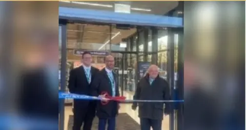 Facebook/David Thomas The three Reform councillors all wearing black jackets, white shirts and pale blue ties. Two are bald, while the third has short dark hair. The one in the middle is holding a pair of giant red scissors as they stand behind a Lidl branded ribbon which has the words 'new store' on it, with the glass doors of Lidl in Cwmbran behind them.