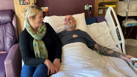 Darren Powell lies on the so-called "cuddle bed" at St Leonard's Hospice in York. His partner Nikki Smith sits on the side of the bed.