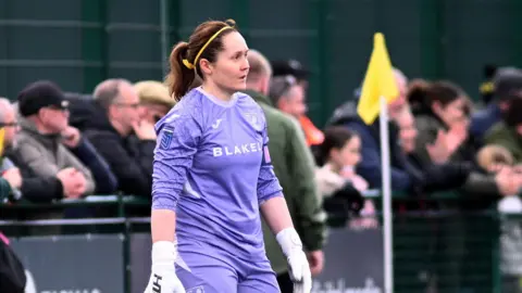 Richard S Brown Sarah Quantrill, wearing a purple Norwich City Women's goalkeeper's kit, stands in her penalty area during a match