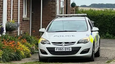 Lincolnshire Police Police car outside a house with flowers adorning the front and fields in the background