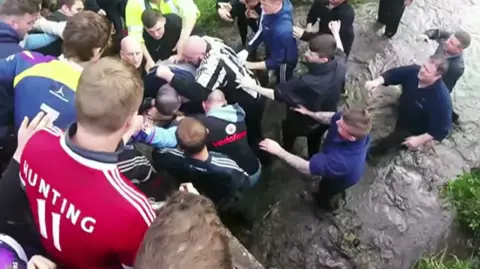 Players inside the beck by the Black Path in a tight scrum, with water up to their knees.